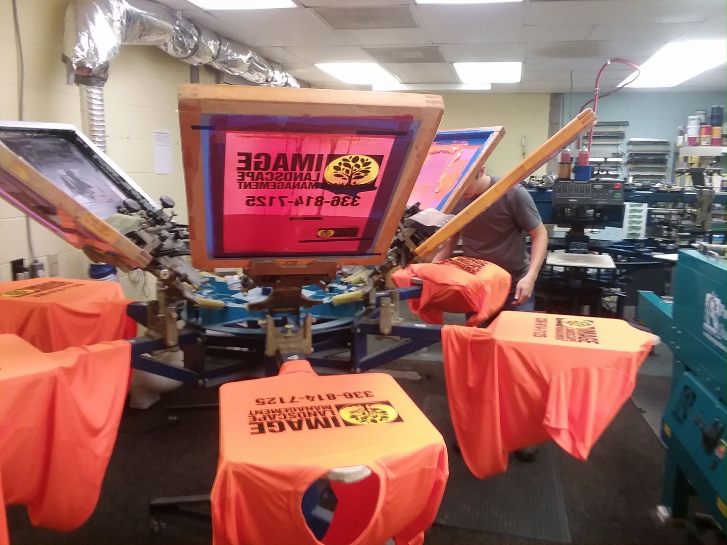 screen printing business A person operates a screen printing machine to print orange T-shirts in a workshop.